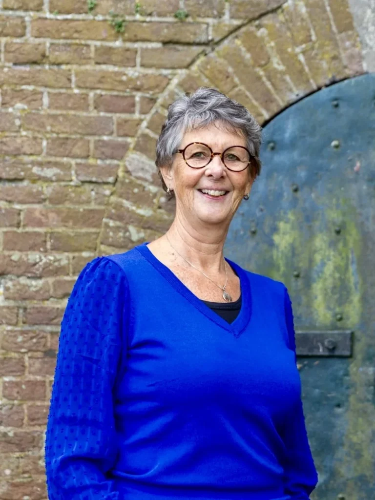 Jeannet Bouman-van Die, eigenaar van Veerkrachtig, lachend voor een oude groene deur in een bakstenen muur